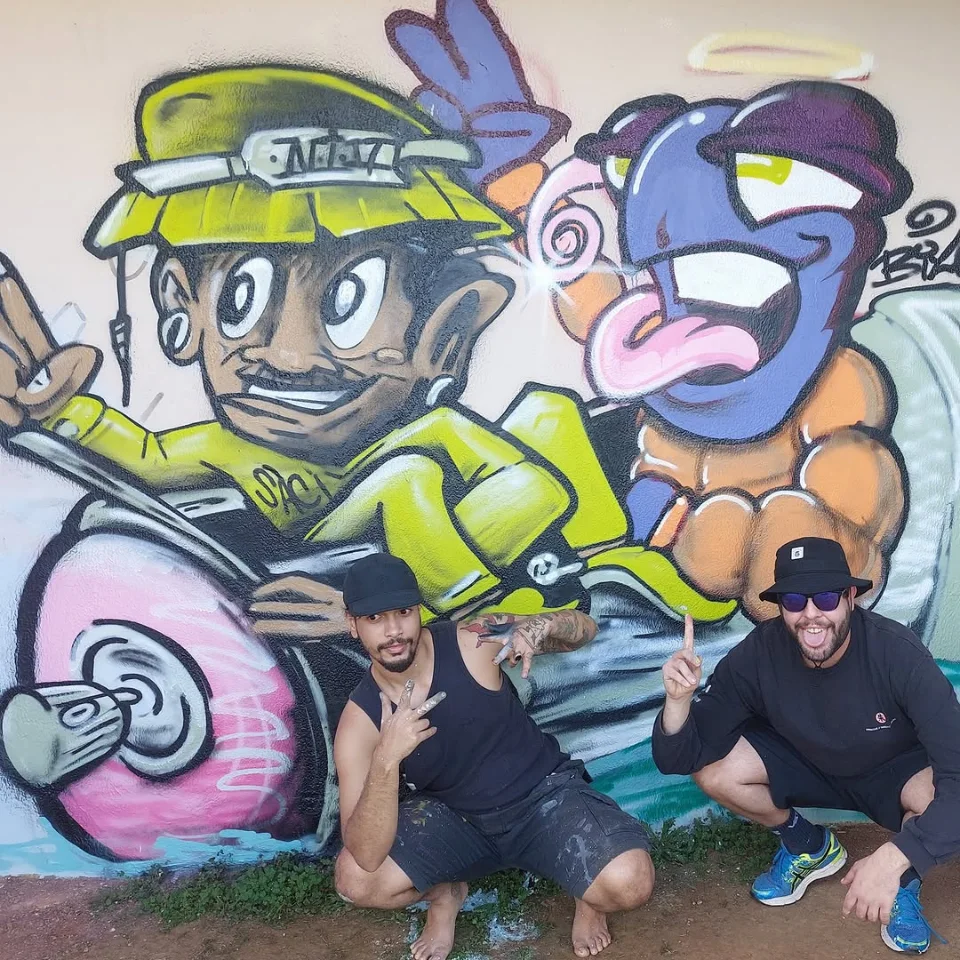 Mural de graffiti com personagens e os artistas em frente ao trabalho